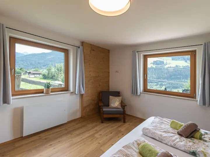 Schlafzimmer mit Holzboden und zwei Fenstern, die einen weiten Blick ins Grüne bieten.