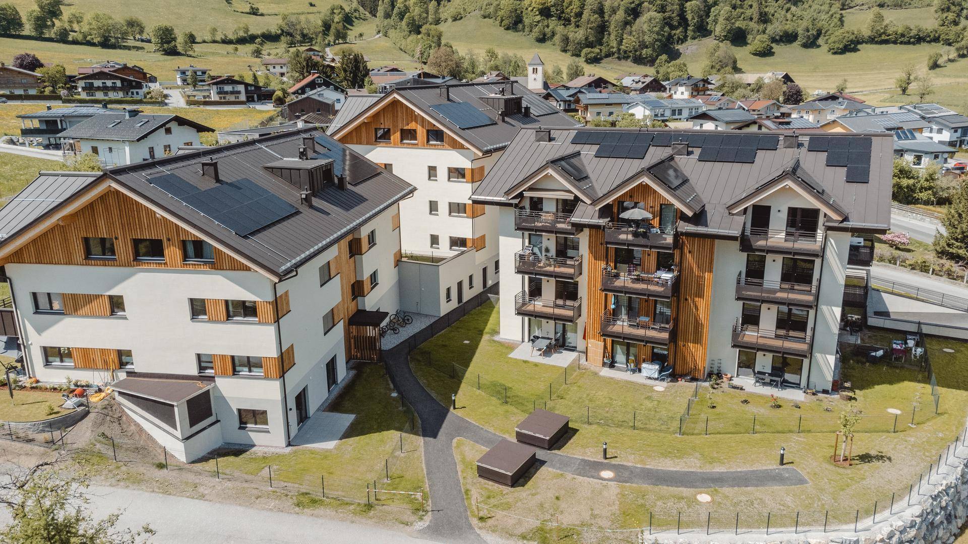 Nahaufnahme einer modernen Wohnanlage mit Holzfassadenelementen, Balkonen und Solaranlagen auf den Dächern.