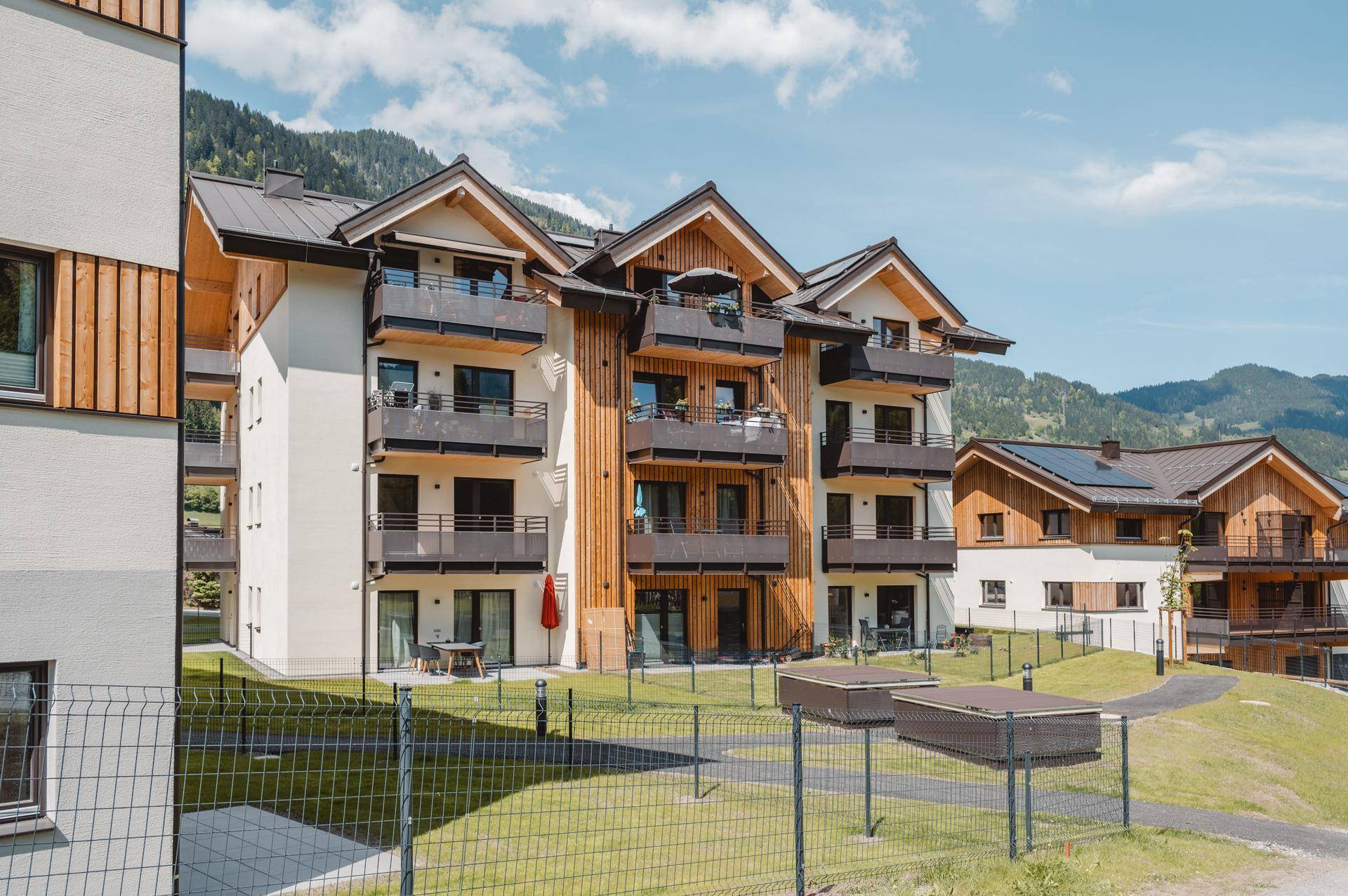 Moderne Wohngebäude mit Holzfassaden, Balkonen und Terrassen, eingebettet in eine bergige Landschaft.