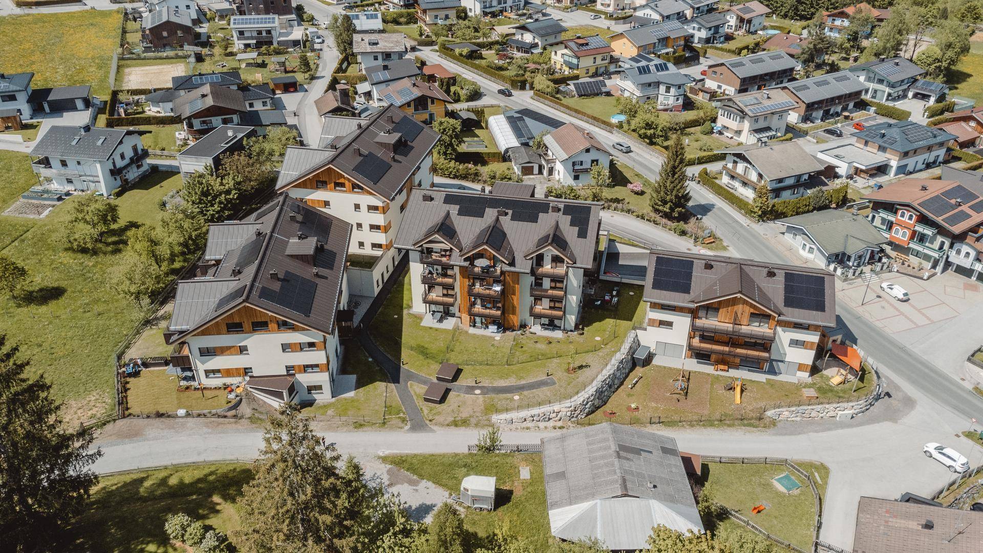 Luftaufnahme einer modernen Wohnanlage mit mehreren Gebäuden, Solaranlagen und Balkonen in ländlicher Umgebung.