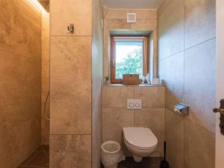 Separates WC mit Wand-WC, Waschbecken und Fenster für natürliche Belüftung und Helligkeit.