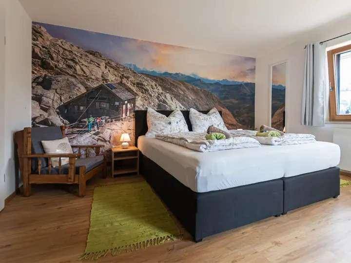 Gemütliches Schlafzimmer mit Doppelbett, Holzboden und Wandtapete mit Bergmotiv für alpine Atmosphäre.