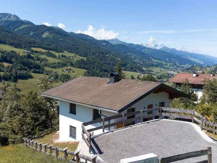 Haus in alpiner Landschaft mit Bergblick und großem Vorplatz, umgeben von grünen Hügeln.