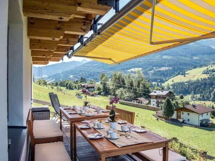 Balkon mit Esstischen, Markise und Panoramablick auf die umliegende Berglandschaft und Natur.
