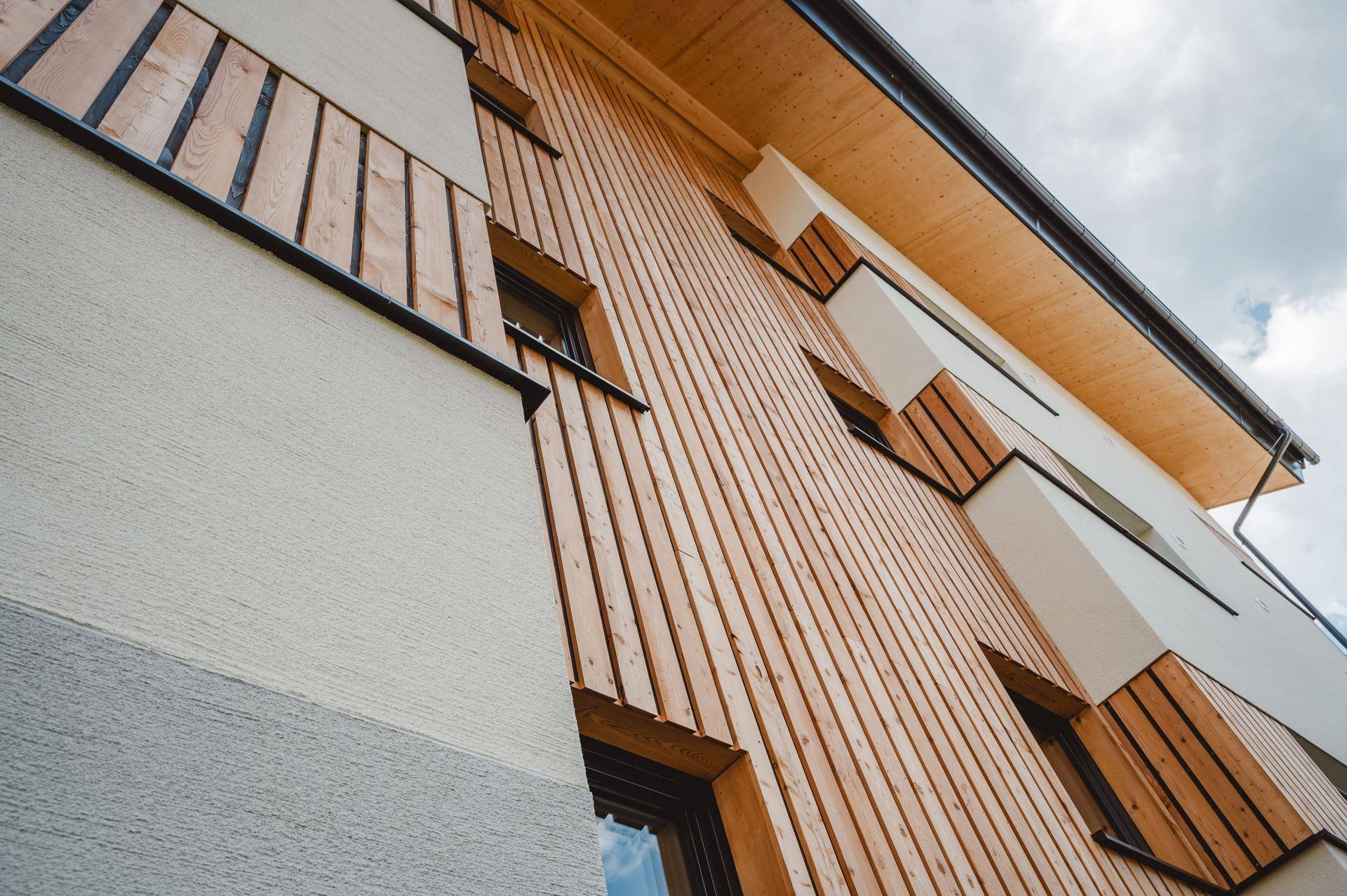 Detailansicht der modernen Fassade mit vertikaler Holzverkleidung und großen Fenstern unter einem Holzdach.