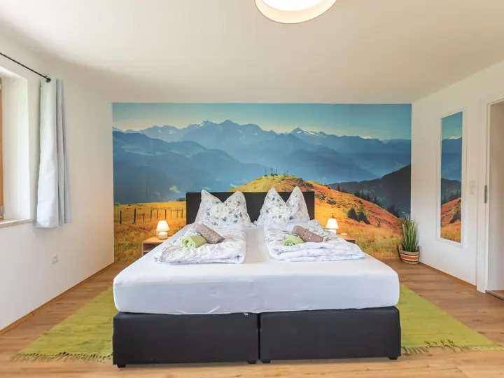 Helles Schlafzimmer mit Doppelbett, Holzboden und Wandtapete mit beeindruckendem Alpenpanorama.