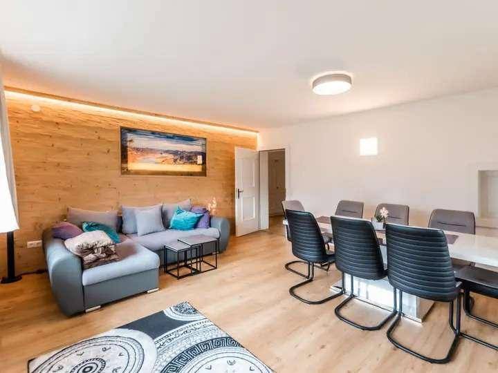 Offener Wohn- und Essbereich mit Holzwand, modernem Sofa und großem Esstisch für gesellige Runden.