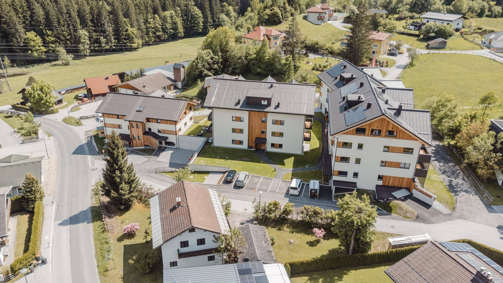 Weitläufige Luftaufnahme eines Wohngebiets mit modernen Gebäuden, umgeben von grüner Natur und Bergen.