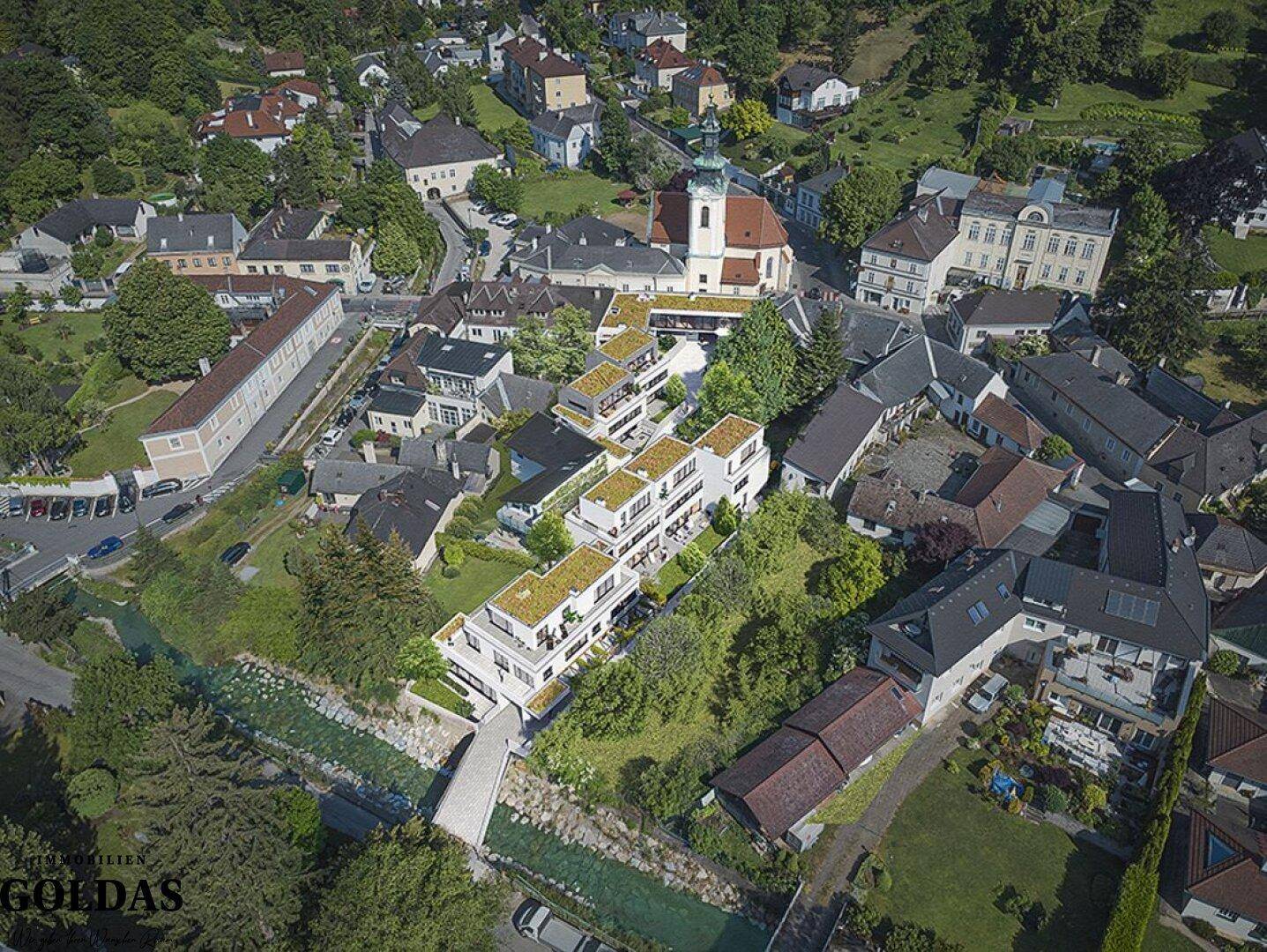 Luftaufnahme einer Wohngegend mit modernen Gebäuden, umgeben von viel Grün und einem Fluss.