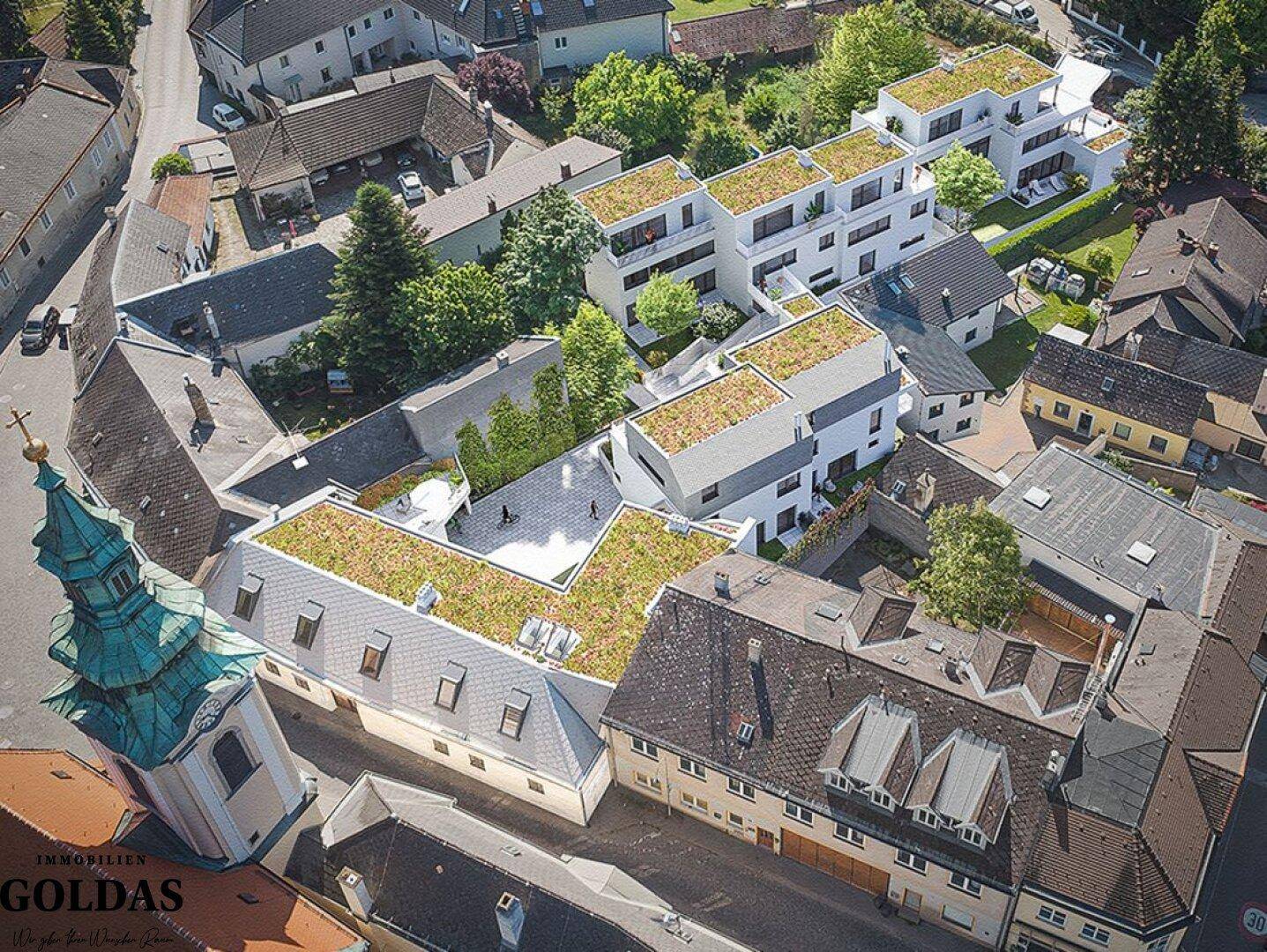 Luftaufnahme eines modernen Wohnkomplexes mit begrünten Dächern und angrenzender historischer Kirche.