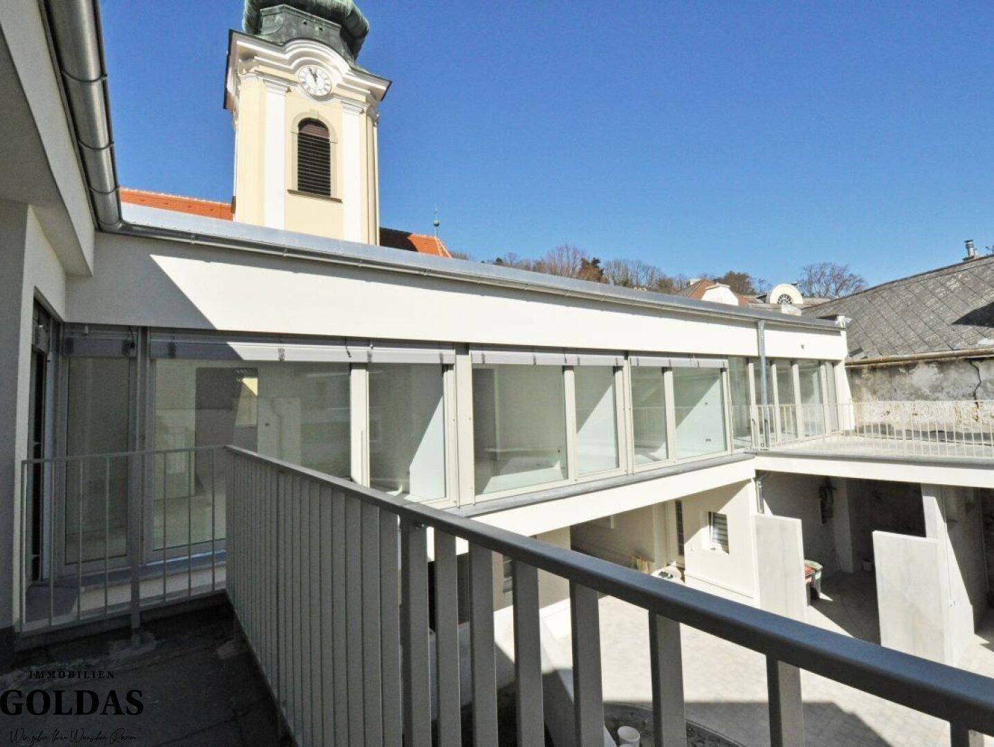Außenbereich mit Balkon und Blick auf die umliegenden Gebäude und einen Kirchturm.
