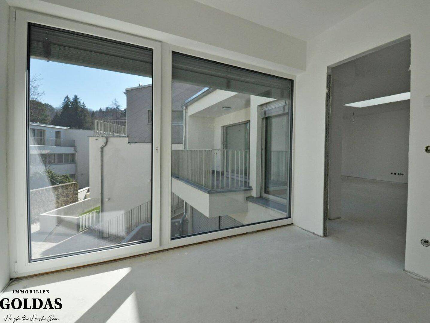 Unmöblierter Raum mit großen Fenstern, die einen Blick auf die moderne Wohnanlage bieten.