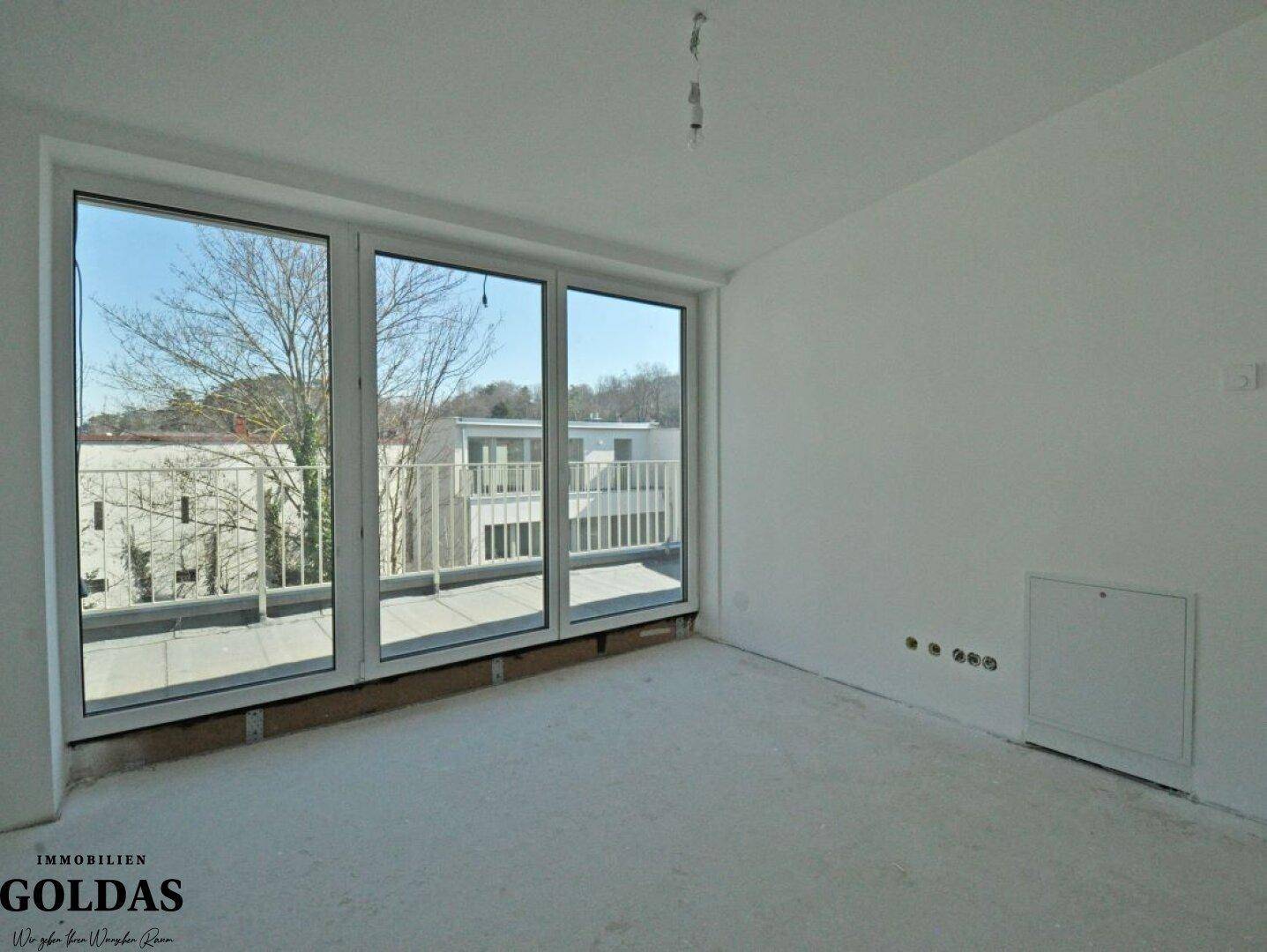 Geräumiger, unmöblierter Raum mit großen Fenstern und Blick auf den gegenüberliegenden Balkon.