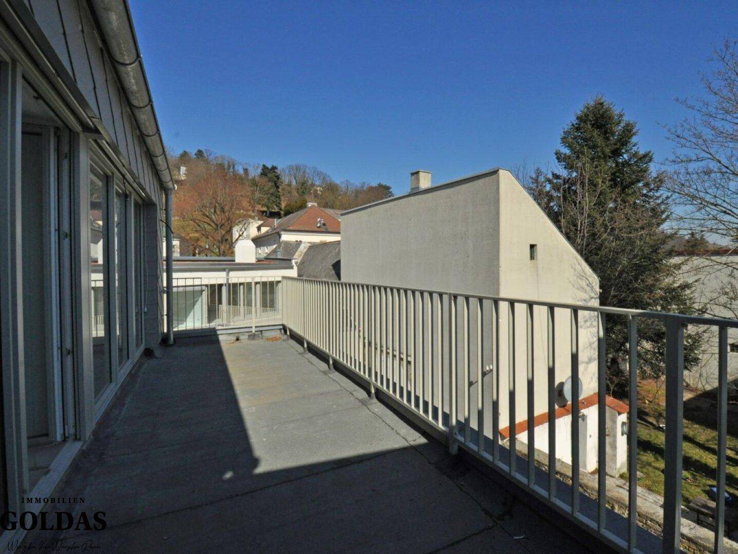 Langer Balkon mit Metallgeländer und seitlichem Blick auf die umliegenden Häuser und Hügel.