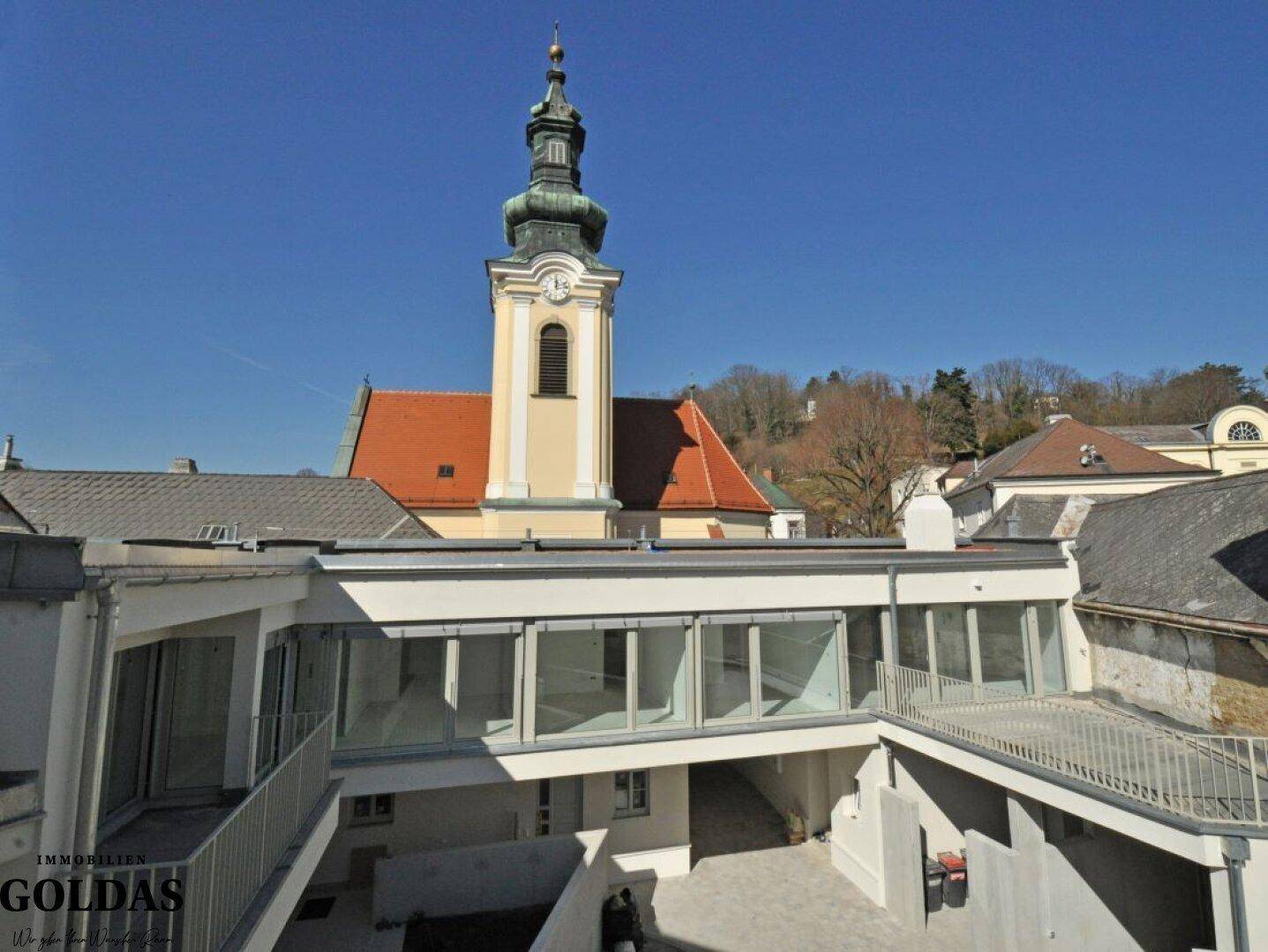 Gesamtansicht der modernen Wohnanlage von oben mit einem historischen Kirchturm im Hintergrund.