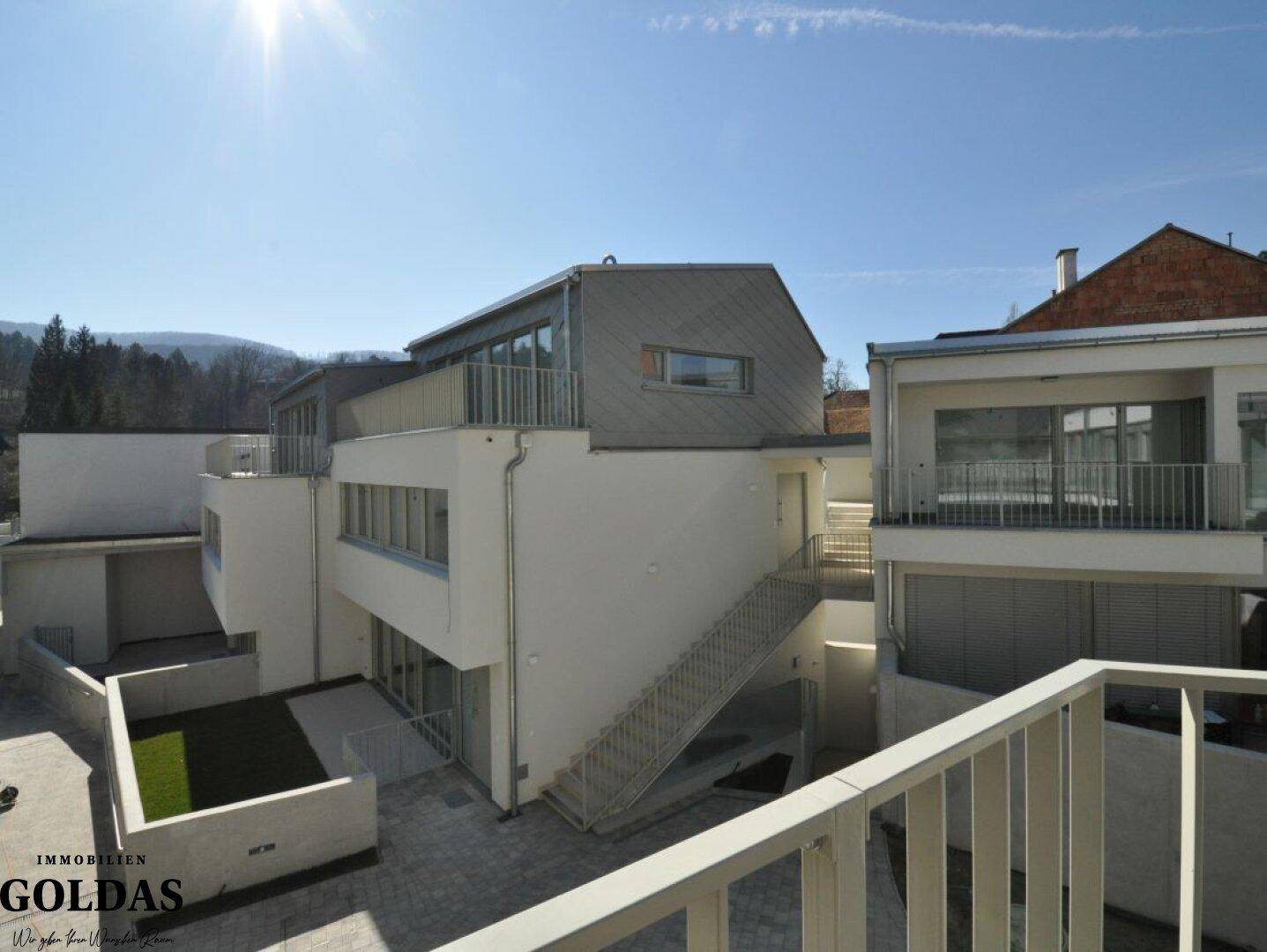 Moderne Wohnanlage mit mehreren Ebenen und Außentreppen unter strahlendem Sonnenschein.