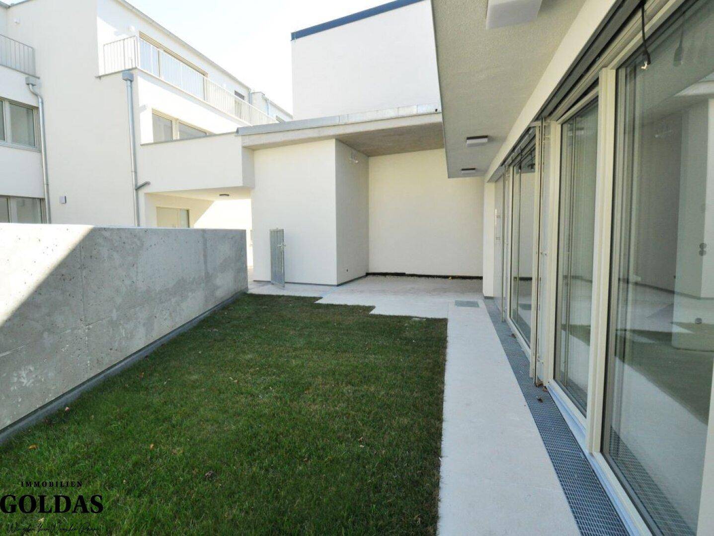 Private Grünfläche mit angrenzender Terrasse und moderner Architektur im Hintergrund.