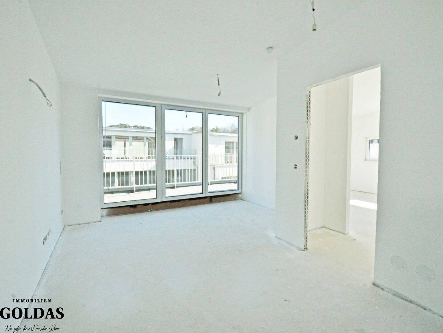 Geräumiger Innenraum mit großen Fenstern, die Zugang zu einem Balkon bieten und viel Licht hereinlassen.