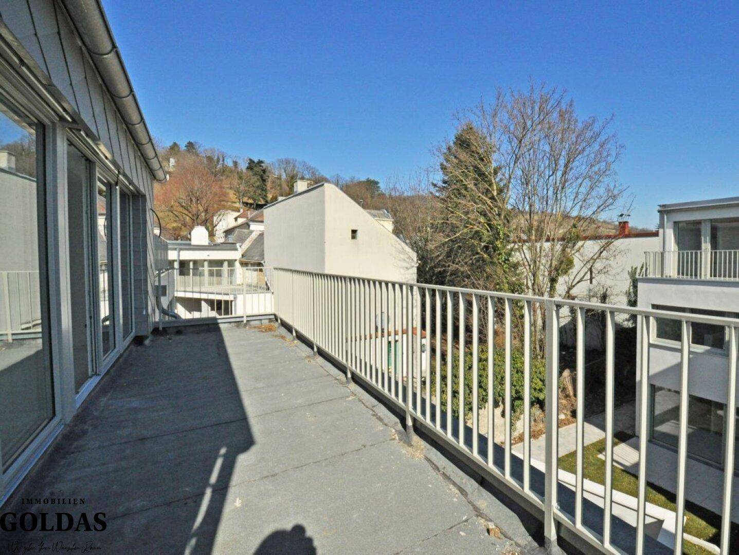 Langer Balkon mit weitem Blick über die grüne Umgebung und die benachbarten Gebäude.