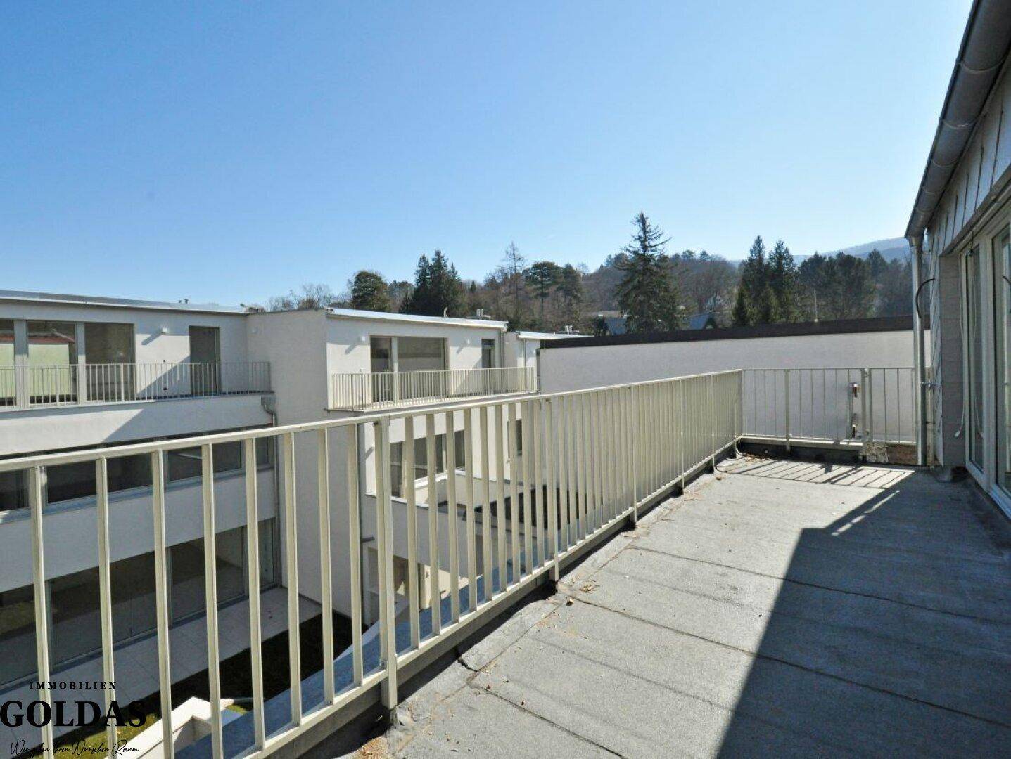 Großer Balkon mit Metallgeländer und Blick auf die umliegenden Gebäude und Bäume.