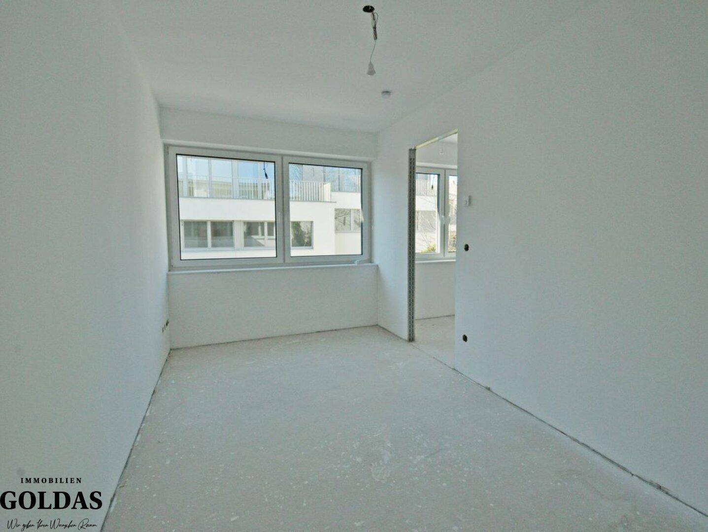 Helles, unmöbliertes Zimmer mit Fenster und Blick auf die umliegenden Gebäude.