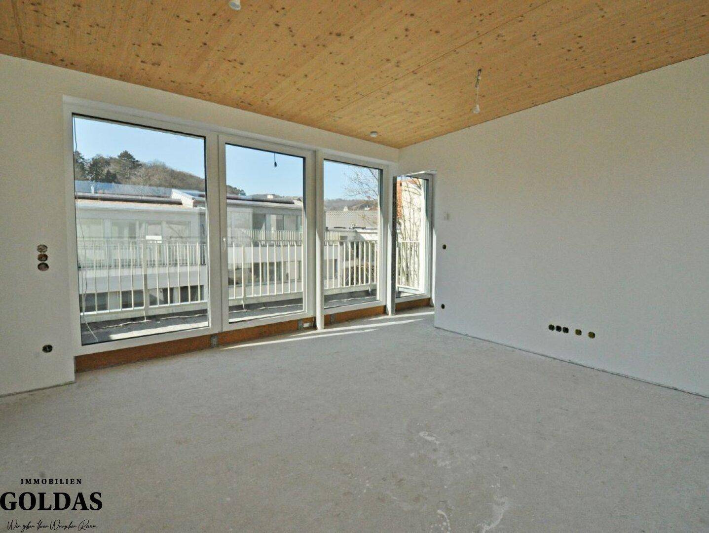 Geräumiges Zimmer mit Holzbalkendecke und großen Fenstern, die viel Tageslicht hereinlassen.
