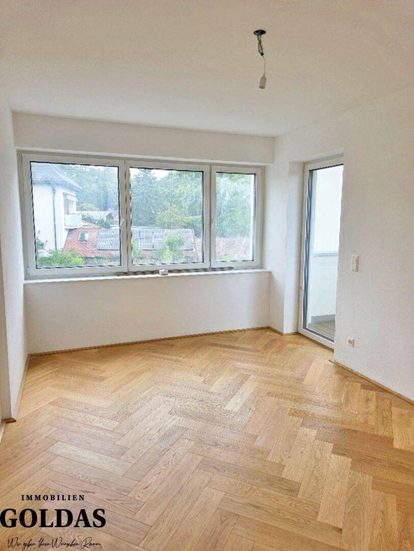 Helles Zimmer mit Parkettboden, großen Fenstern und Zugang zu einem französischen Balkon.