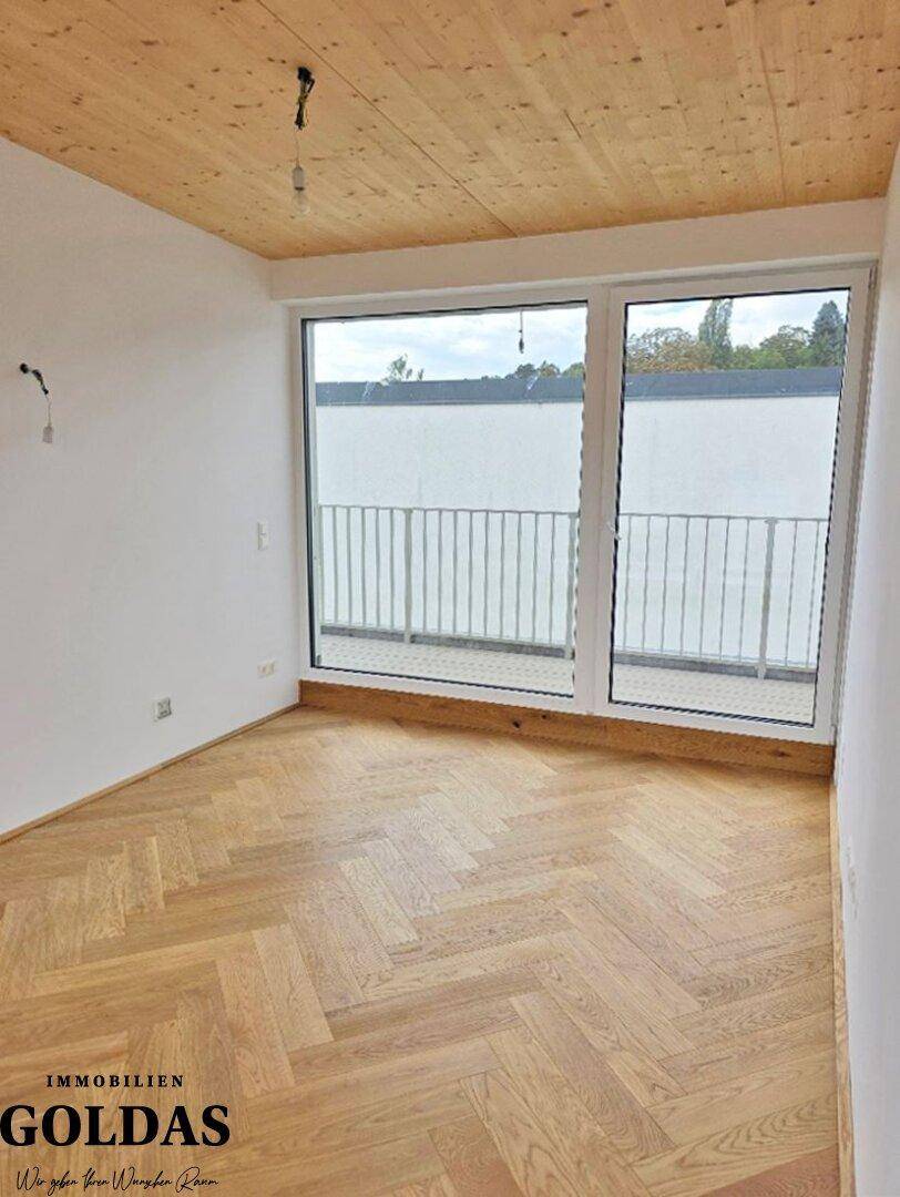 Helles Zimmer mit Holzbalkendecke, Parkettboden und großen Fenstern mit Balkonzugang.