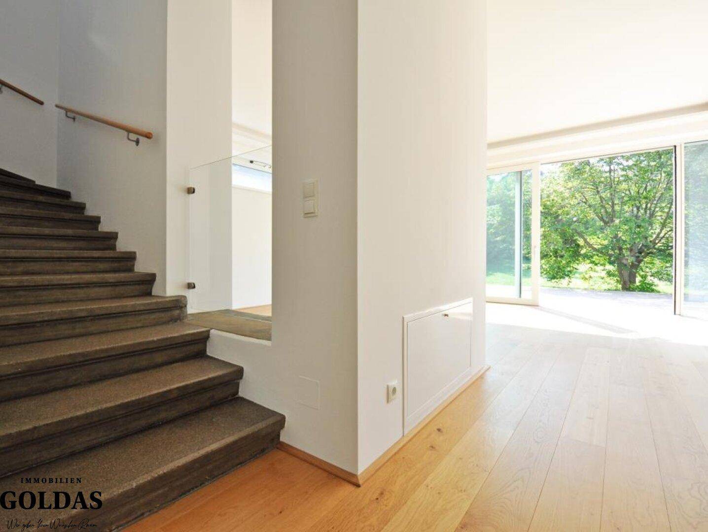 Heller Flur mit Steintreppe und Holzboden, der zu einem lichtdurchfluteten Raum führt.