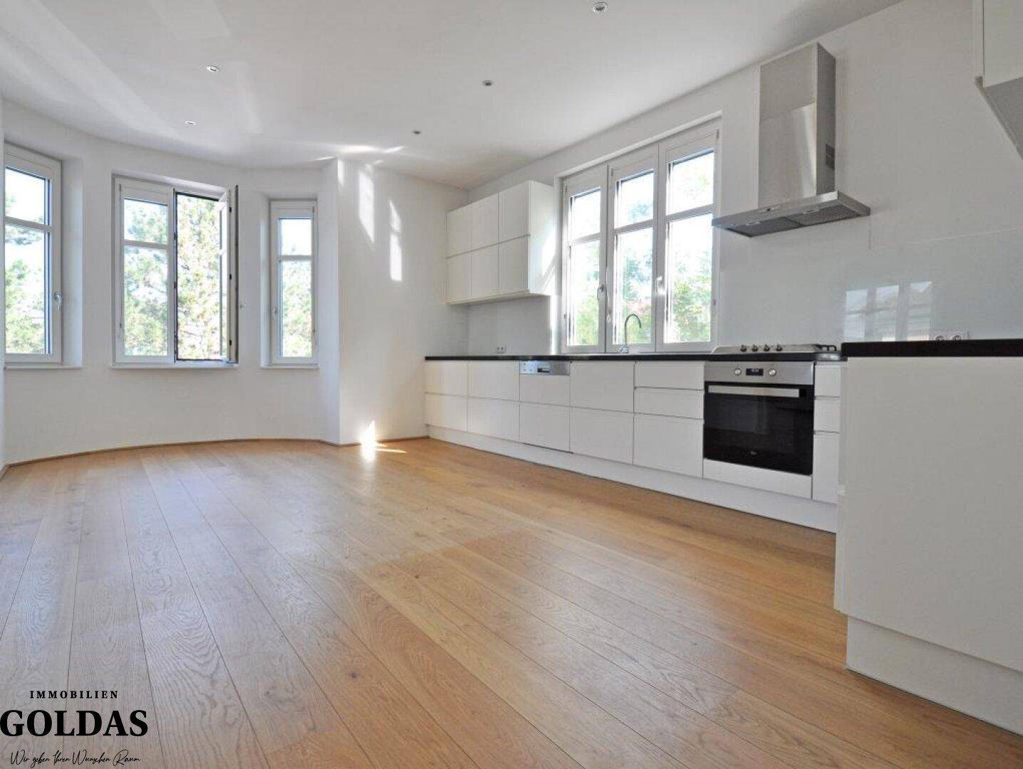 Moderne, helle Küche mit weißen Schränken, Holzboden und großen Fenstern.