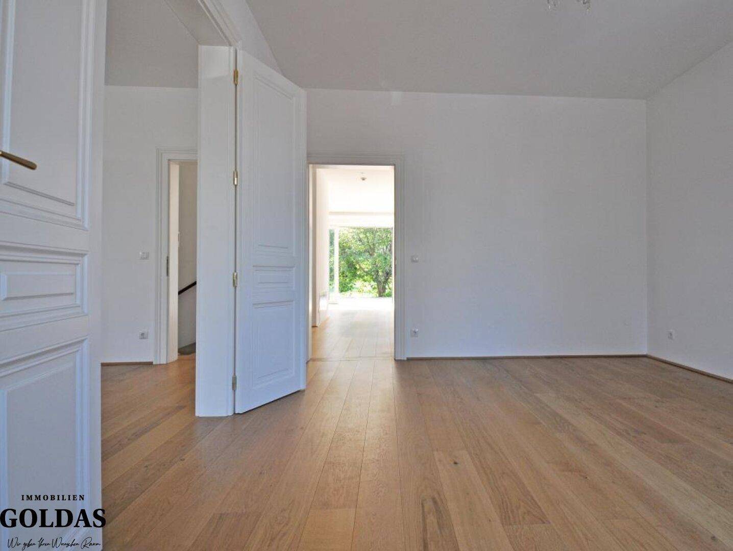 Heller Wohnbereich mit Holzboden und Zugang zu anderen Räumen, lichtdurchflutet.