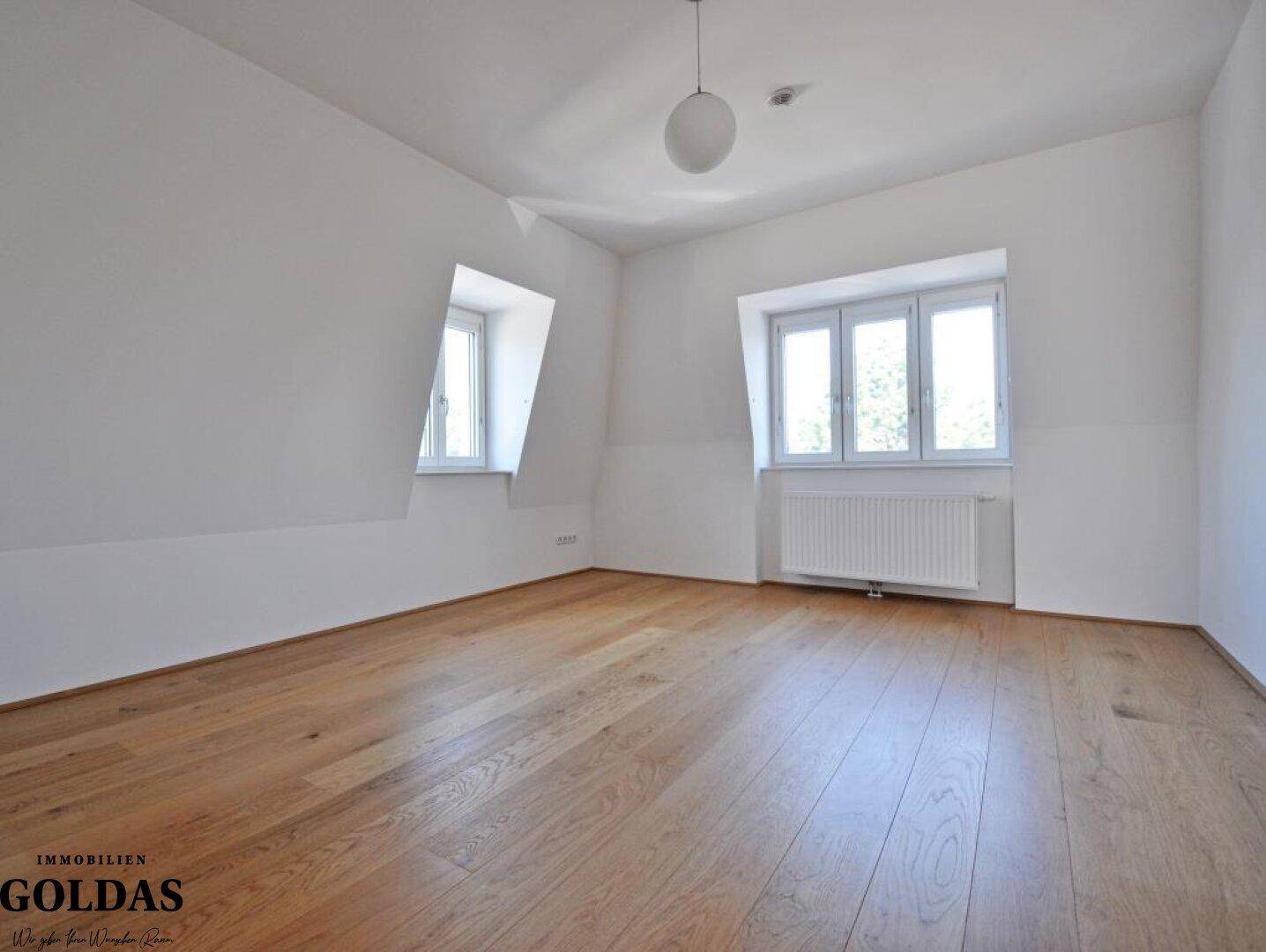 Helles Schlafzimmer im Dachgeschoss mit Holzboden, Dachschrägen und Fenstern.