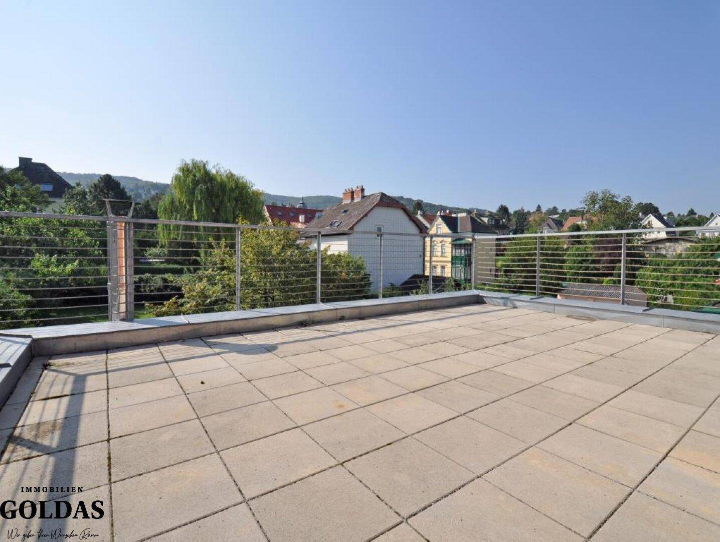Weitläufige Dachterrasse mit Fliesen und modernem Geländer, umgeben von viel Grün.