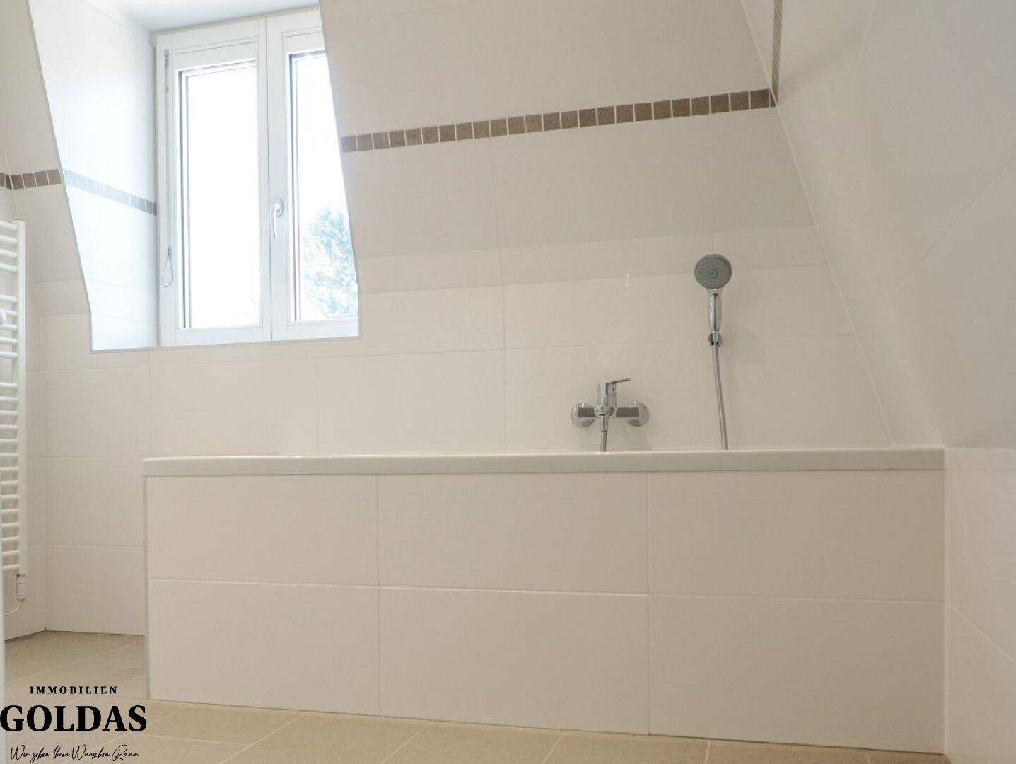 Modernes Badezimmer mit Badewanne, weißen Fliesen und Fenster im Dachgeschoss.