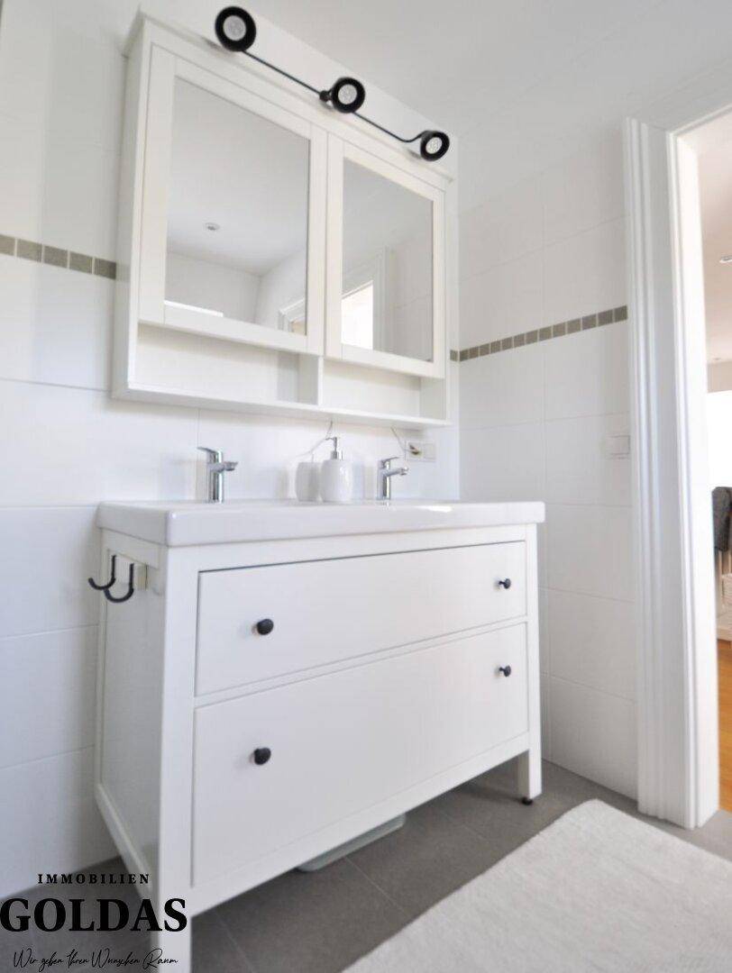 Helles Badezimmer mit Doppelwaschbecken, Spiegelschrank und weißen Fliesen.