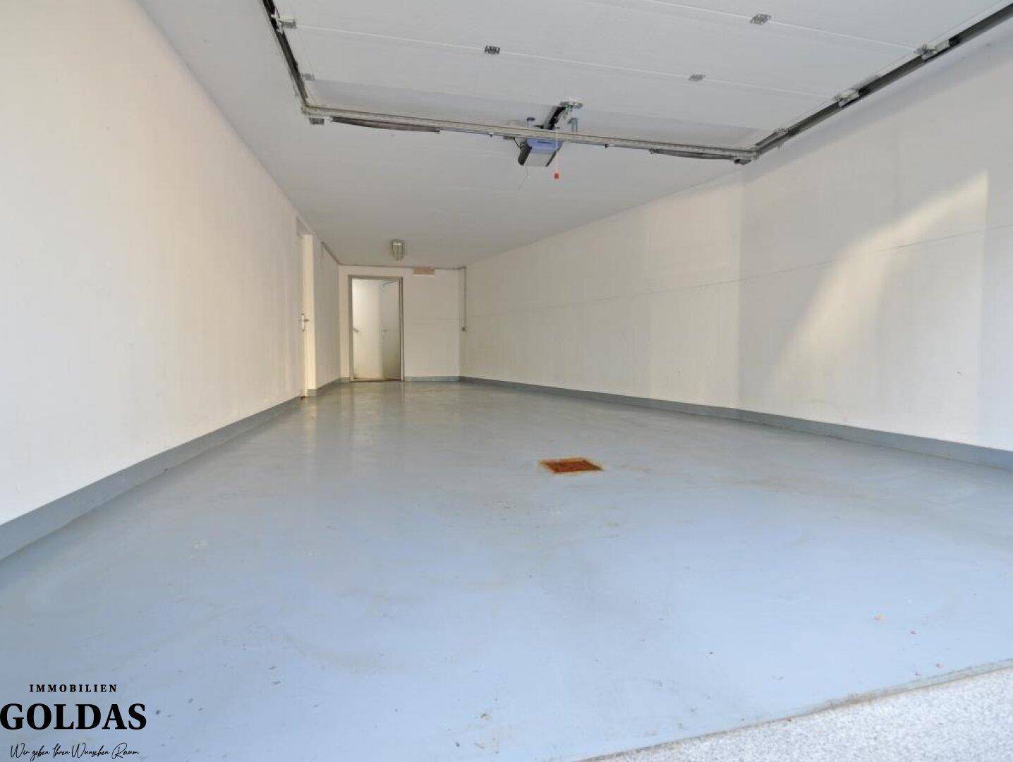 Lange Garage mit glattem Boden und Zugang zu einem weiteren Raum, gut beleuchtet.