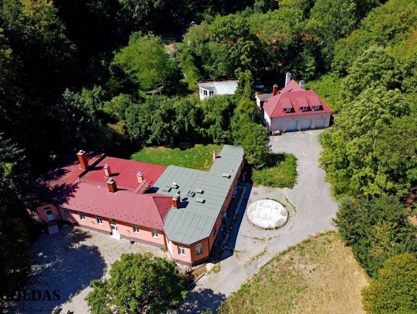 Nahaufnahme des Hauptgebäudekomplexes von oben, mit roten und grauen Dächern und gepflastertem Bereich.