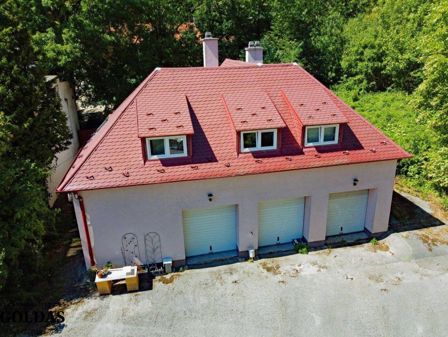 Nebengebäude mit drei Garagentoren und roten Dachziegeln, umgeben von Bäumen und einem Vorplatz.
