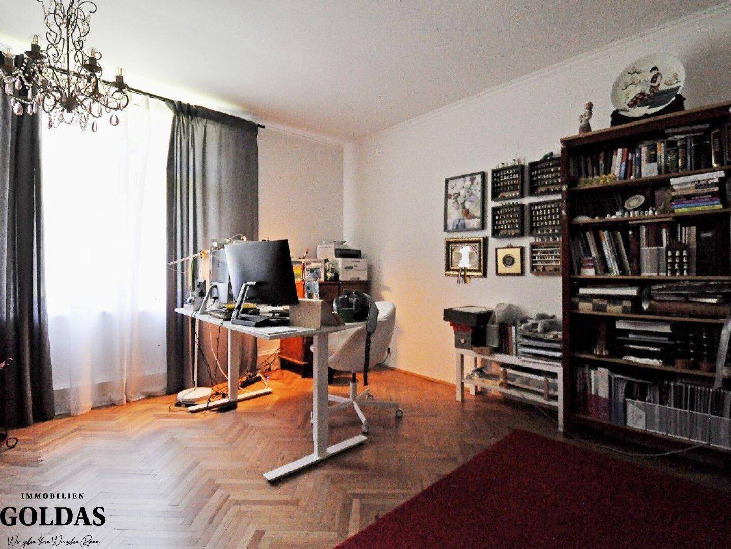 Arbeitszimmer mit Parkettboden, Bücherregal und Schreibtisch am Fenster.
