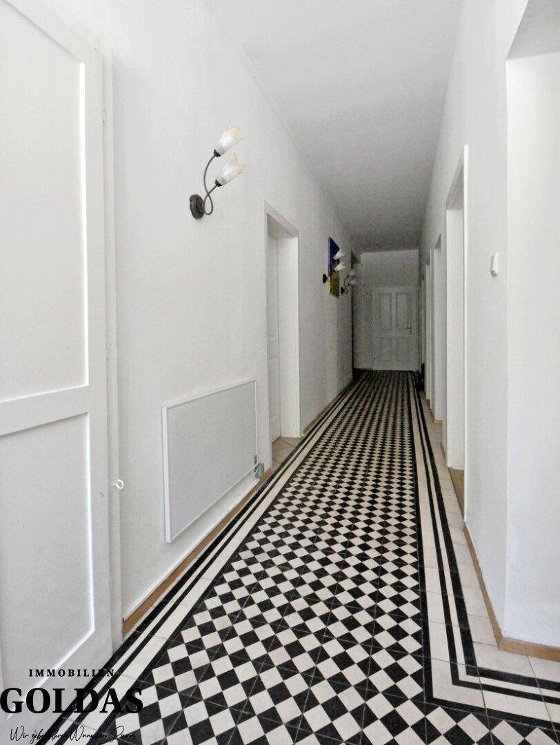 Langer Flur mit schwarz-weißem Schachbrettmuster-Fliesenboden und weißen Wänden.