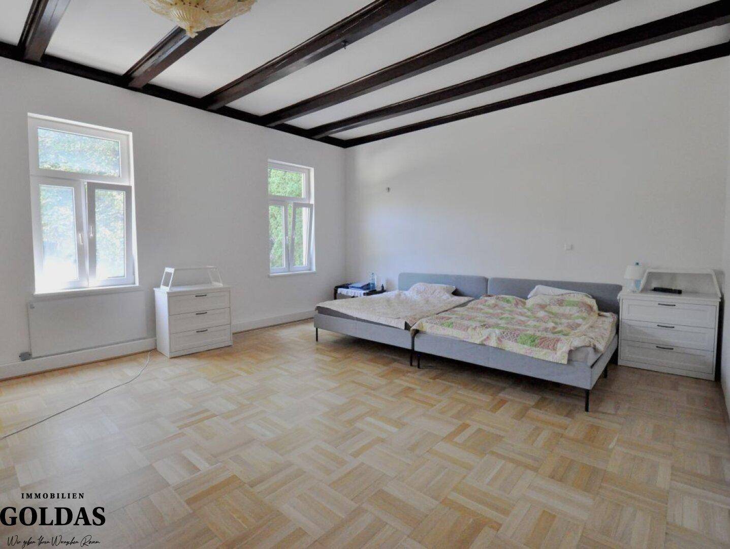 Helles Schlafzimmer mit Holzbalkendecke, Parkettboden und zwei Einzelbetten.