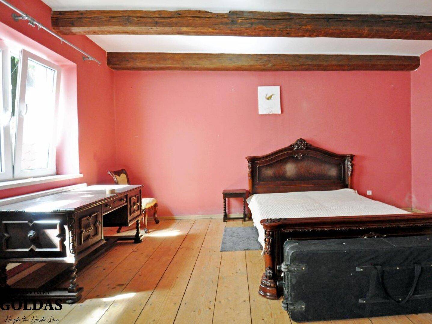Geräumiges Schlafzimmer mit Holzbalken, Dielenboden und einem großen Holzbett.