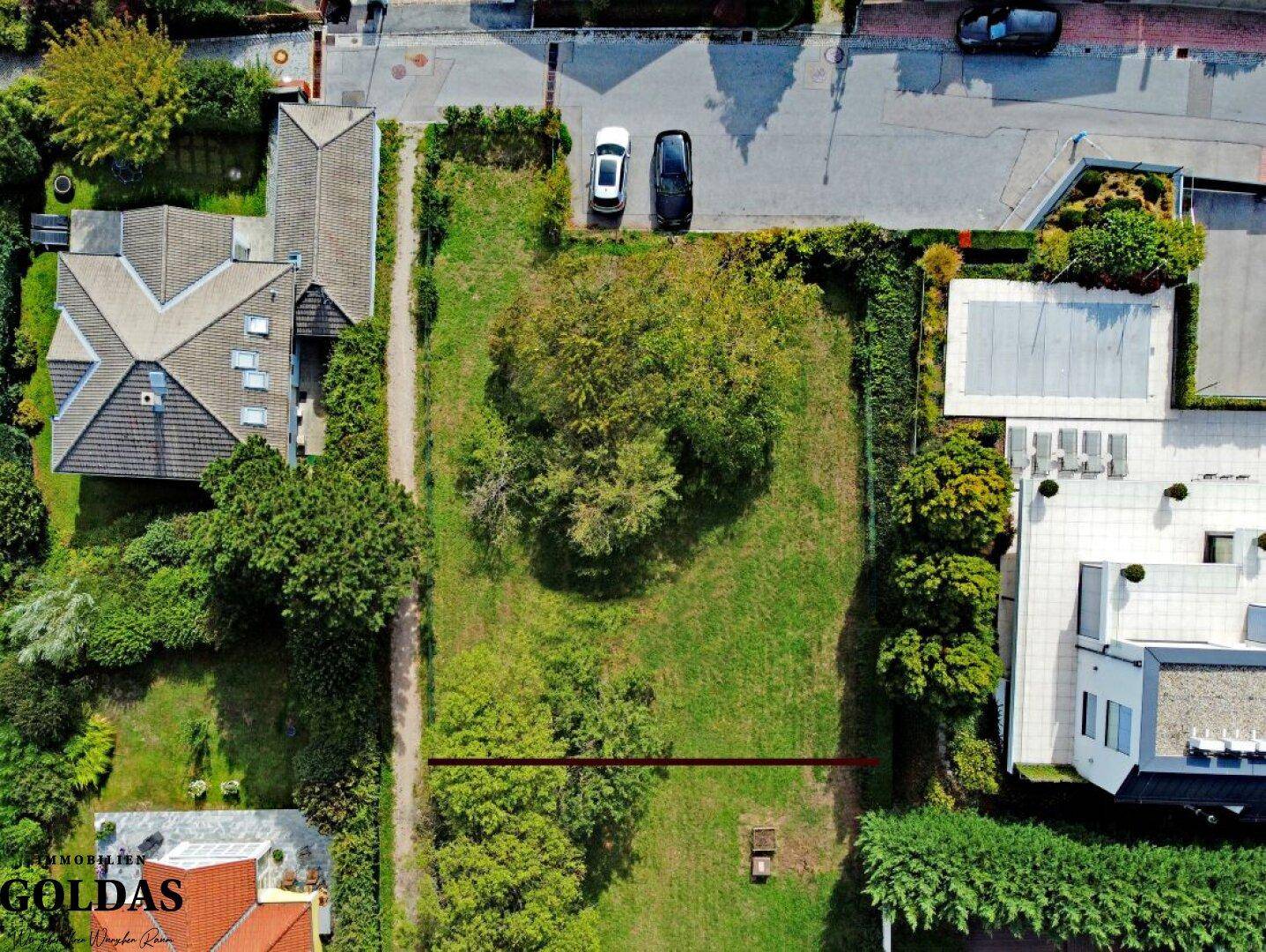 Luftbild des großen Baugrundstücks mit viel Grün und angrenzenden modernen Gebäuden.