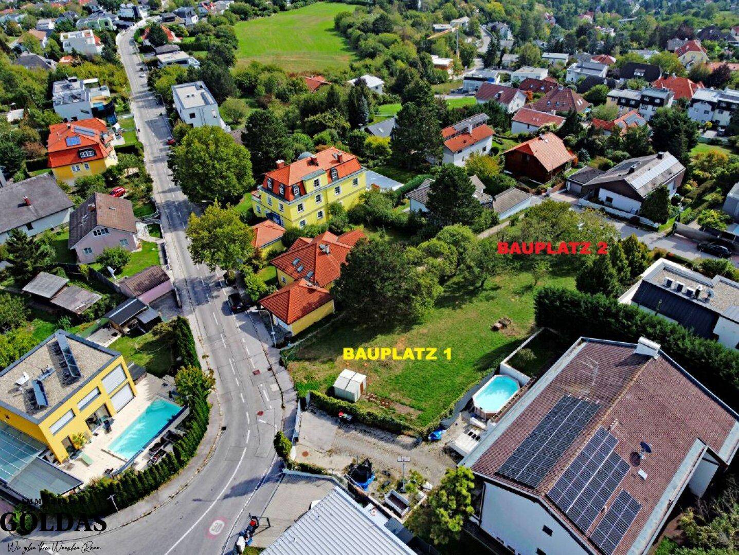 Weitläufige Luftaufnahme des Baugrundstücks mit umliegender Wohnbebauung und grüner Landschaft im Hintergrund.