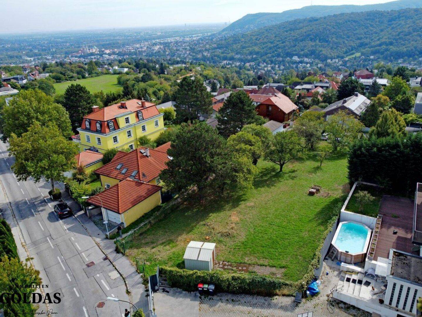 Nahaufnahme aus der Luft eines Baugrundstücks umgeben von Wohnhäusern und viel Grün.
