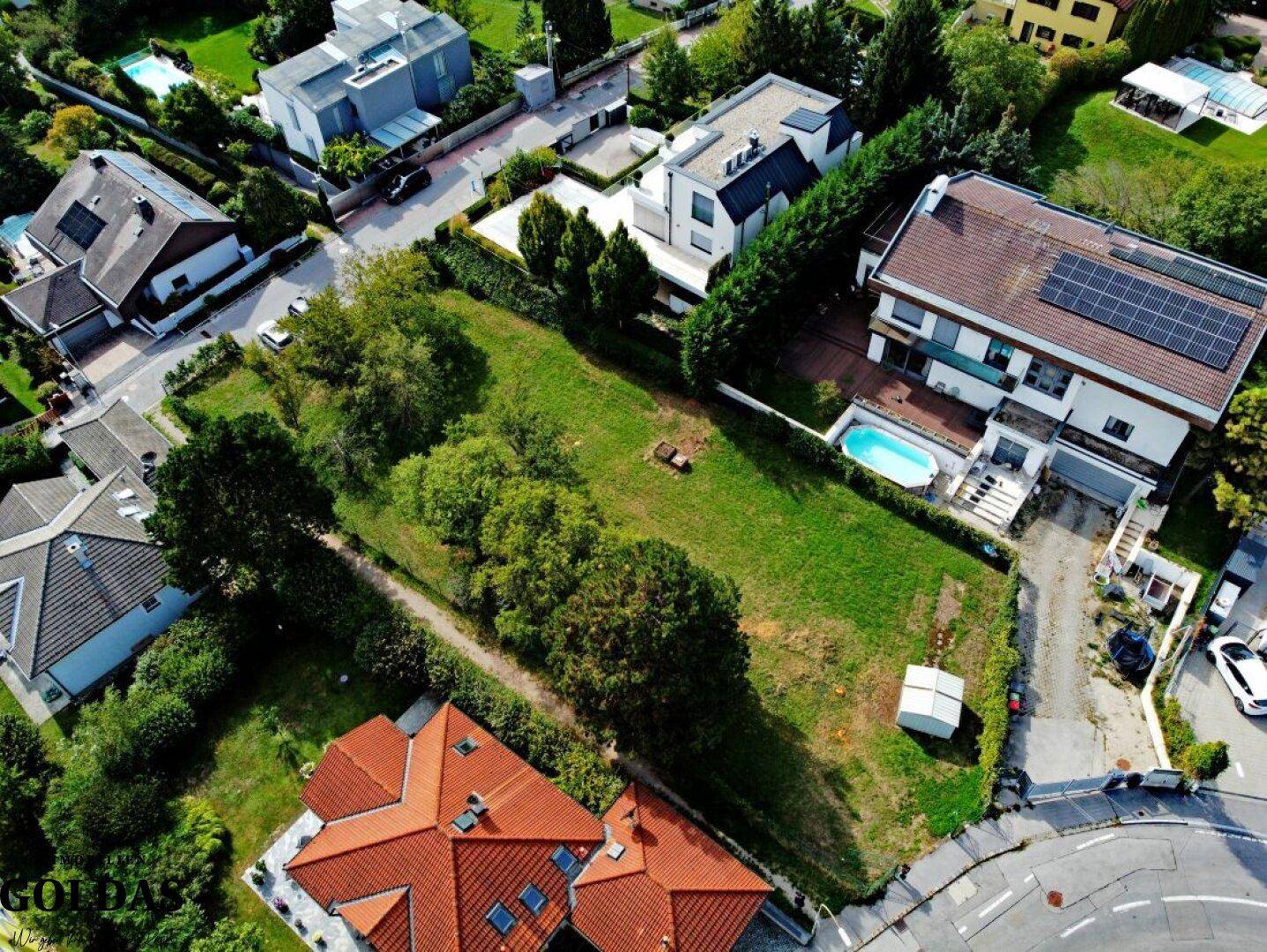 Luftaufnahme des Baugrundstücks mit angrenzenden modernen Häusern und einem Pool.
