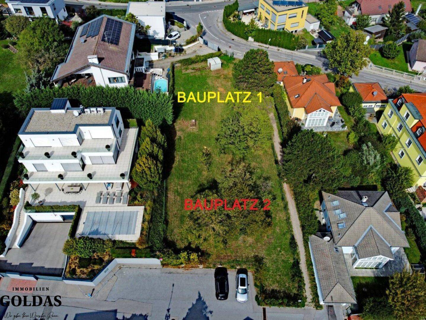 Luftaufnahme des Baugrundstücks, unterteilt in zwei Bauplätze, mit angrenzenden modernen Gebäuden.