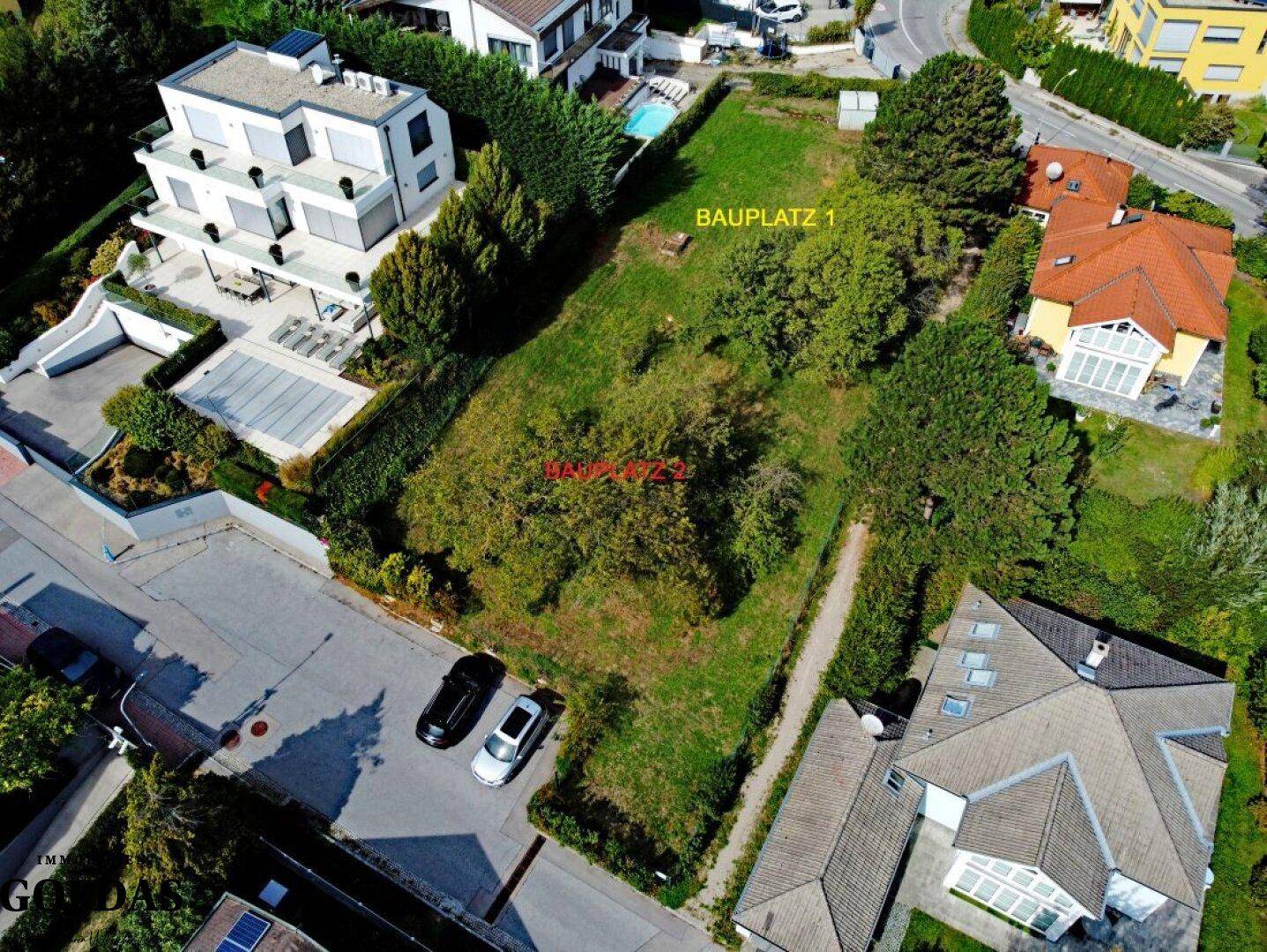 Überblick aus der Luft über das Baugrundstück, mit markierten Bereichen für zwei Bauplätze, umgeben von Häusern.