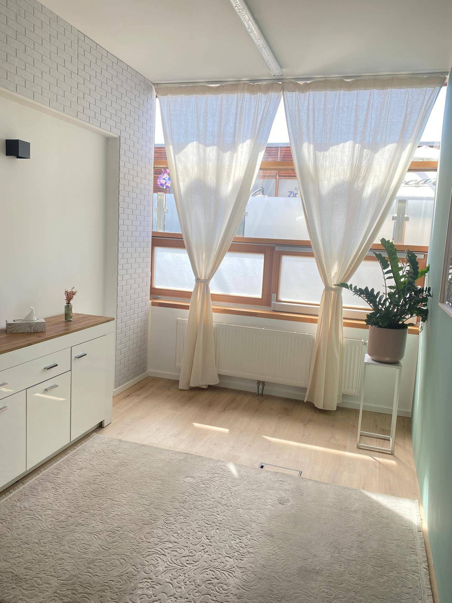 Heller Raum mit Holztheke, Pflanze und großen Fenstern mit weißen Vorhängen.