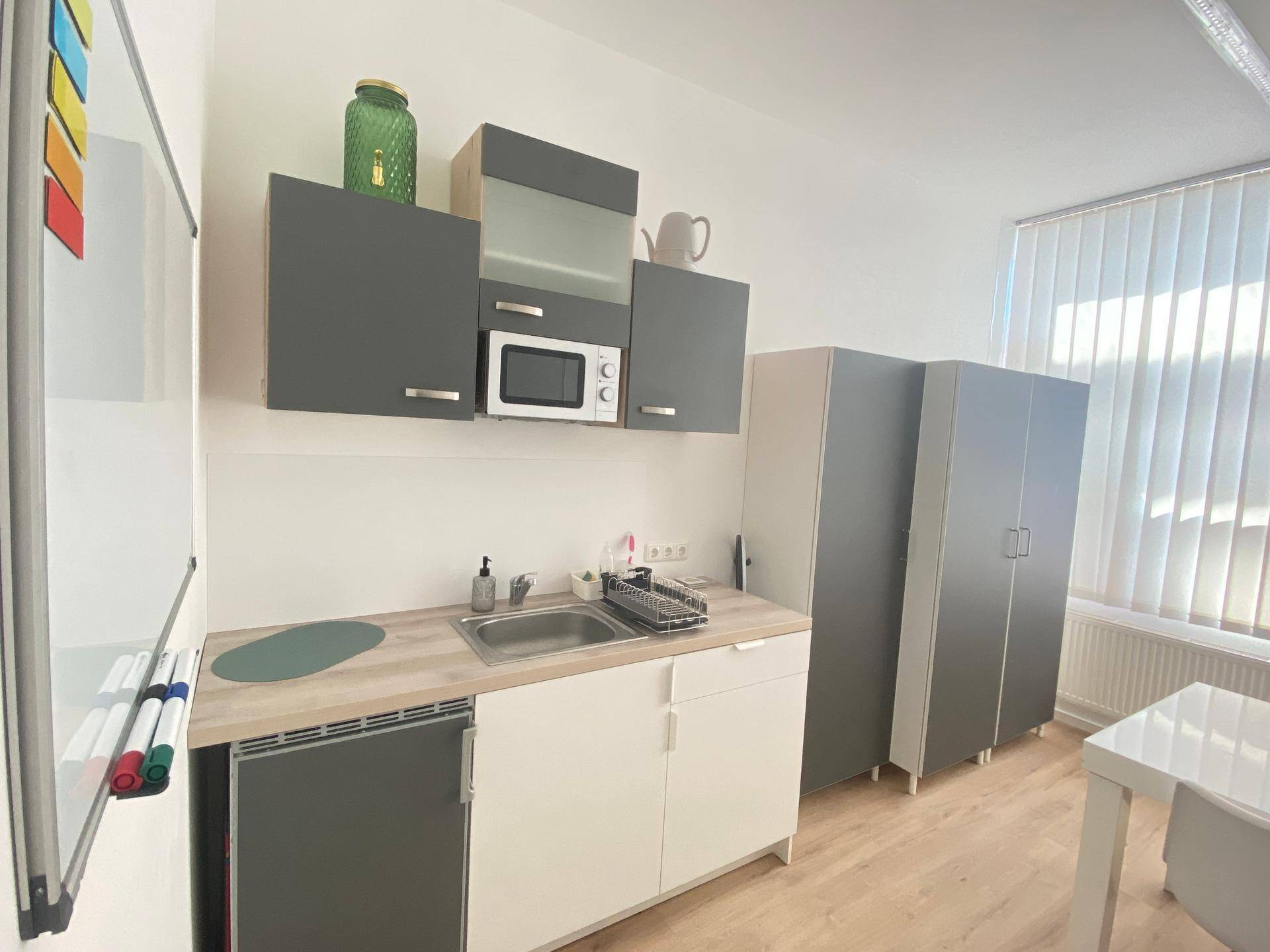 Kleine Küchenzeile mit Mikrowelle, Spüle und Kühlschrank in einem hellen Raum.